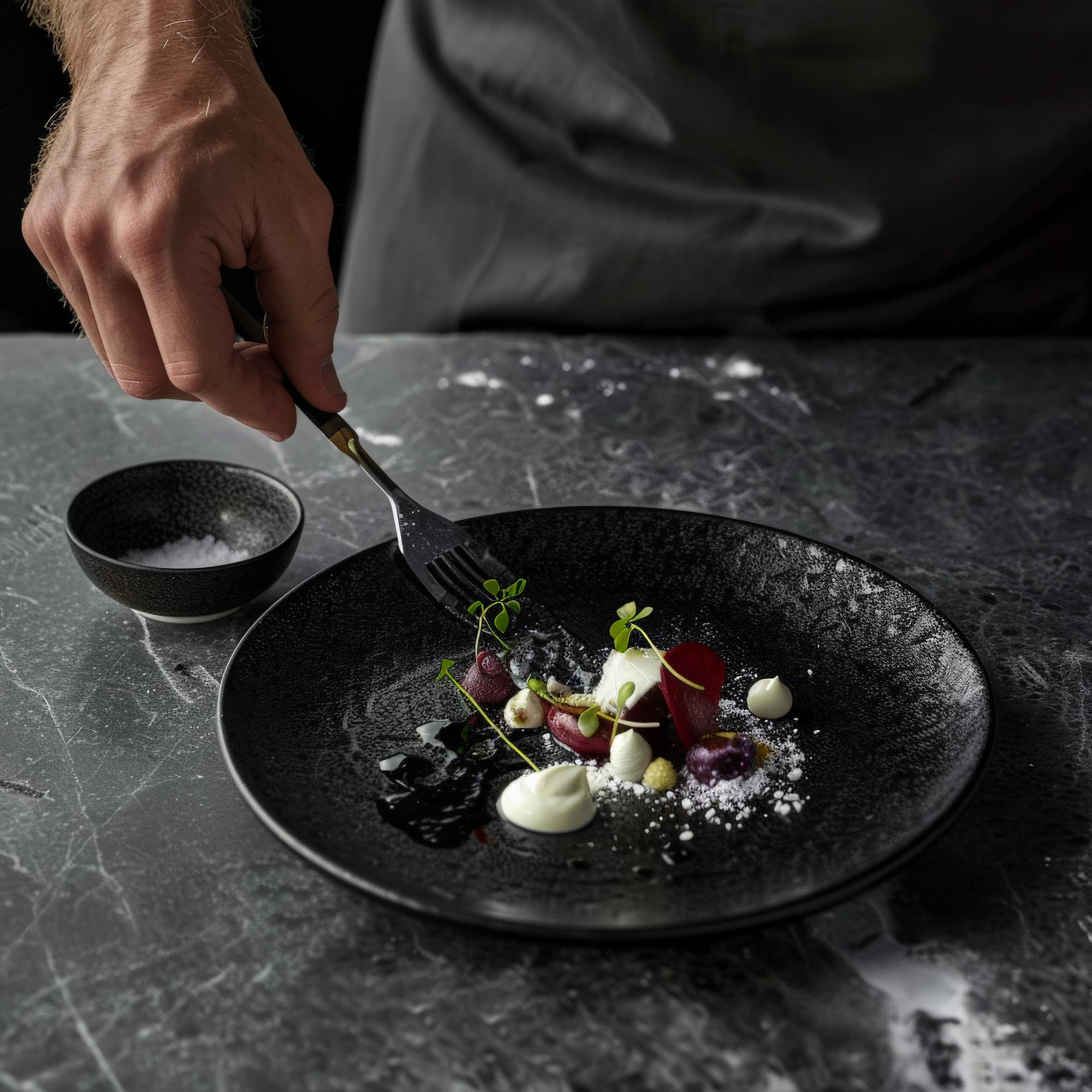 Chef preparing a plated gourmet dish in a dark elegant kitchen